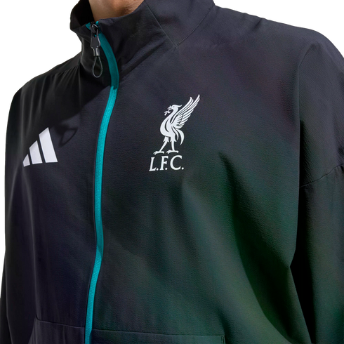 Close-up of a dark Adidas jacket featuring a teal zipper and the white Liverpool F.C. crest on the chest.