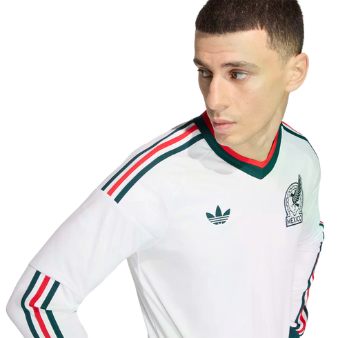 Man wearing a white Mexico national team long-sleeve jersey with green and red stripes and the team crest, posed against a solid black background.