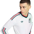 Man wearing a white Mexico national team long-sleeve jersey with green and red stripes and the team crest, posed against a solid black background.