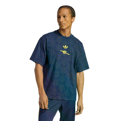 A man modeling a navy blue Adidas x Arsenal t-shirt with a geometric pattern and yellow logos, paired with navy track pants against a black background.