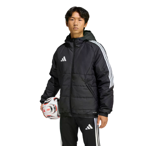 Man wearing a black Adidas puffer jacket and tracksuit pants, holding a soccer ball against a solid black background.