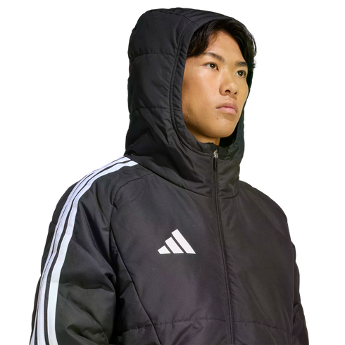 Young man wearing a black Adidas hooded puffer jacket with white stripes on the sleeve and a white logo on the chest against a black background.