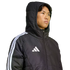 Young man wearing a black Adidas hooded puffer jacket with white stripes on the sleeve and a white logo on the chest against a black background.