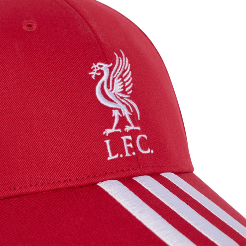 Close-up of a red baseball cap with a white embroidered Liverpool FC Liver Bird logo and "L.F.C." text, featuring three white stripes on the brim.