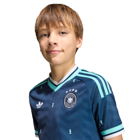 A smiling boy with light brown hair wears a navy blue German soccer jersey with teal stripes and an Adidas logo against a solid black background.