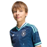 A smiling boy with light brown hair wears a navy blue German soccer jersey with teal stripes and an Adidas logo against a solid black background.