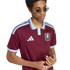 A person with sunglasses and rings wears a maroon and light blue Adidas Aston Villa polo shirt against a plain white background.