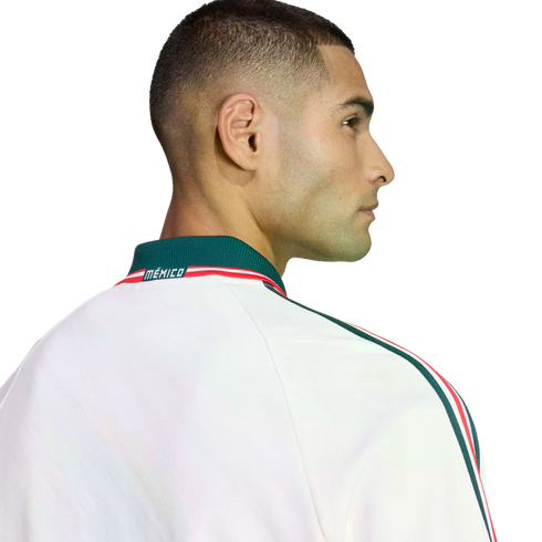 Profile of a man with a buzz cut wearing a white Mexico jacket with green and red trim, set against a black background.