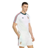A man models a white Adidas football kit with green and red striped accents on the sleeves and shorts, featuring a gold team crest, against a solid black background.