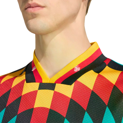 Close-up of a person wearing a vibrant harlequin-patterned jersey in red, yellow, black, and teal, featuring a German flag-colored striped collar.