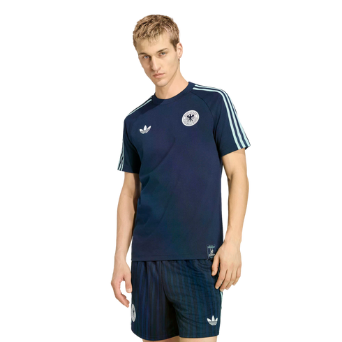 A man wearing a navy blue Adidas Germany national football team t-shirt and matching shorts, standing against a solid black background.