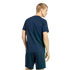 Back view of a man with blonde hair wearing a navy blue t-shirt and matching striped shorts against a black background.