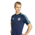 Young man with short blonde hair wearing a navy blue Adidas Germany t-shirt with mint green stripes, looking down and to the side against a black background.