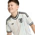 A young person smiling in a white Adidas Japan football jersey with vertical rainbow stripes, set against a solid black background.