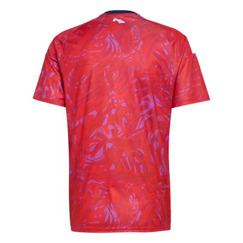 Back view of a red short-sleeved jersey with a purple abstract swirled pattern. A small white script logo is centered below the dark blue collar line.