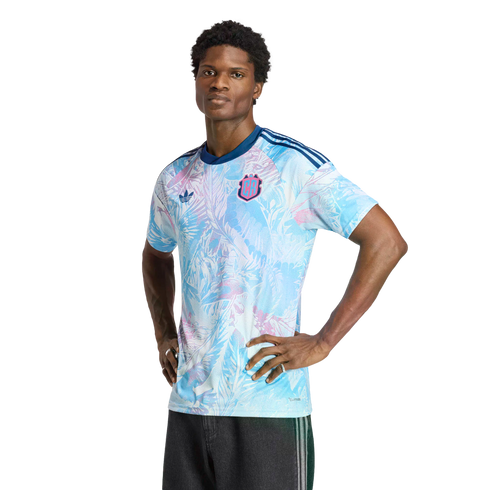 A man models a light blue and pink floral-patterned Adidas jersey with a 'CR' crest, standing with his hands on his hips against a solid black background.