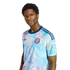 A man models a light blue and pink tropical-print Adidas jersey with a "CB" crest against a black background.