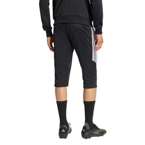 Rear view of an athlete wearing black three-quarter length soccer training pants with white side stripes and black soccer cleats against a plain background.