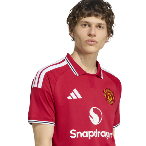 A young man wearing a red Manchester United home jersey with a white collar and Snapdragon sponsor logo against a white background.