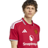 A young man wearing a red Manchester United home jersey with a white collar and Snapdragon sponsor logo against a white background.
