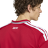 Close-up from behind of a man wearing a red jersey with three white stripes on the shoulder and "UNITED" printed on the back neck.