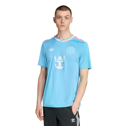 A man models a light blue Inter Miami CF soccer jersey with pink accents and black Adidas pants against a white background.