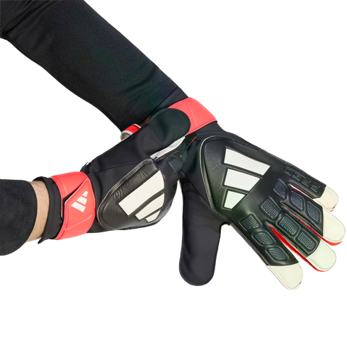 Hands in black, red, and white Adidas goalkeeper gloves against a black backdrop. One hand adjusts the wrist strap of the other.