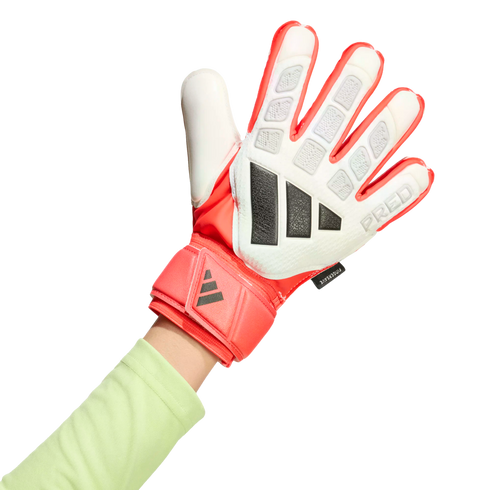 A hand wearing a red and white Adidas Predator goalkeeper glove with black details and a light green long-sleeved shirt against a black background.