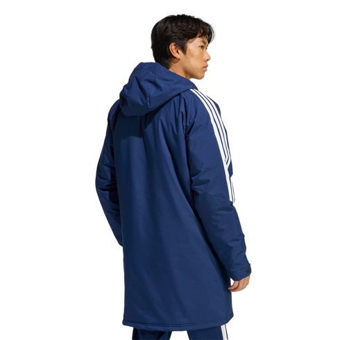 Rear three-quarter view of a man wearing a long navy blue hooded parka featuring three white stripes on the sleeves.
