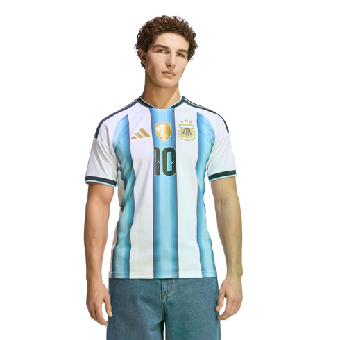 A man with curly hair wearing an Argentina soccer jersey with the number 10 and blue jeans, posed against a black background.