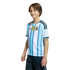 A smiling boy wearing an Argentina national football team jersey with the FIFA World Champions 2022 patch, set against a black background.