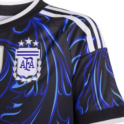 Close-up of a black Argentina soccer jersey with blue abstract patterns, three white shoulder stripes, and the AFA crest topped with three stars.