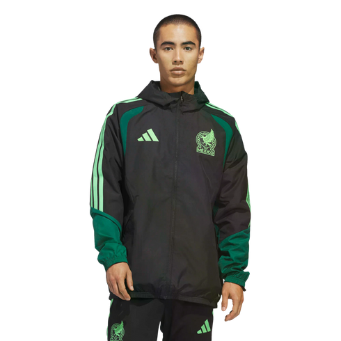 A man wearing a black and green Adidas Mexico National Team windbreaker and matching pants stands against a black background. The jacket features light green team and brand logos.