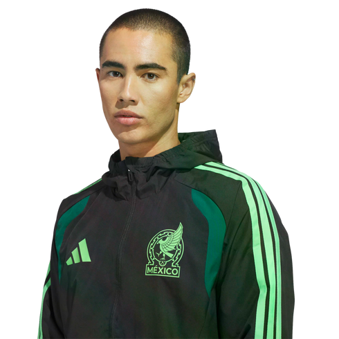A man wearing a black Adidas Mexico national team jacket with bright green accents against a black background.