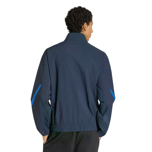 Back view of a person with dark curly hair wearing a navy blue track jacket with bright blue sleeve accents and black pants, set against a solid black background.