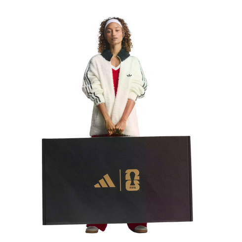 A woman in a white Adidas jacket holds a large black box featuring gold Adidas and FIFA World Cup 26 logos.