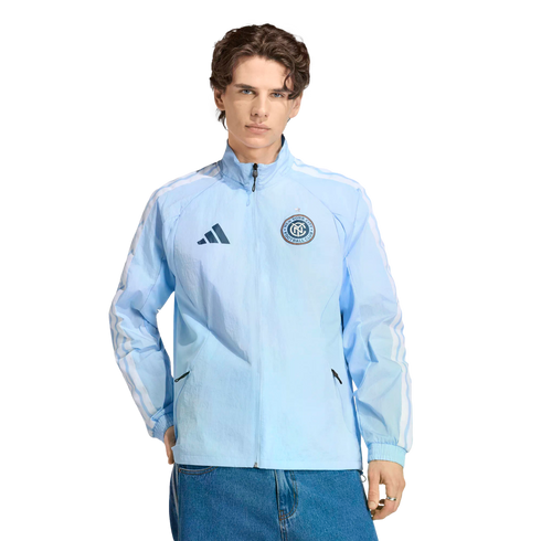 A man wearing a light blue Adidas New York City FC windbreaker and blue jeans against a black background.