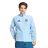 A man wearing a light blue Adidas New York City FC windbreaker and blue jeans against a black background.