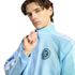 A man with dark wavy hair wears a light blue New York City Football Club zip-up jacket, posing against a black background.