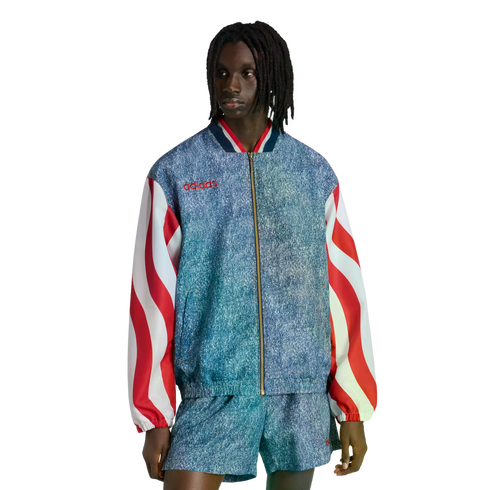 A person with dreadlocks models a blue acid-wash Adidas jacket with red and white wavy striped sleeves and matching shorts against a black background.
