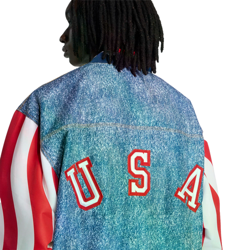 Back view of a person with dreadlocks wearing a denim jacket with red and white striped sleeves and large red "USA" lettering across the back.