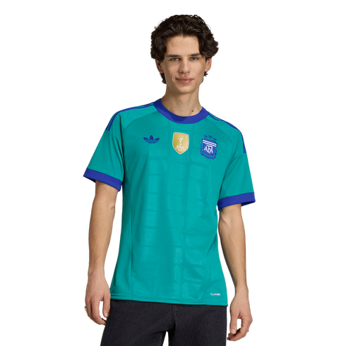 A man wearing a teal Argentina soccer jersey with purple trim, featuring the AFA crest and FIFA World Champions patch, against a black background.