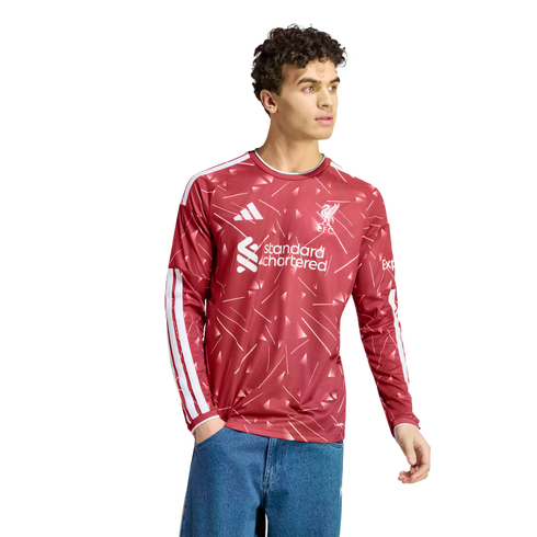 A young man wearing a red long-sleeved Liverpool FC jersey with white patterns and logos, paired with blue jeans, set against a white background.