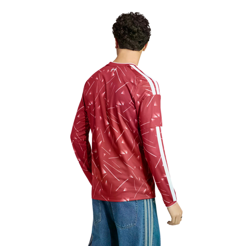Rear view of a man wearing a red patterned long-sleeve jersey with white stripes and blue denim jeans against a white background.