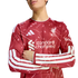 A person wearing a red Liverpool FC long-sleeve Adidas jersey with white patterns, arms crossed against a white background.