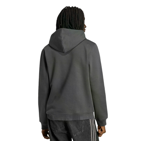 Rear view of a person with dark dreadlocks wearing a dark grey hoodie and black pants with side stripes, standing against a black background.