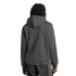 Rear view of a person with dark dreadlocks wearing a dark grey hoodie and black pants with side stripes, standing against a black background.