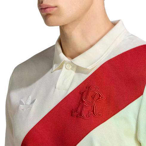 A person wearing a white textured Adidas polo shirt with a red diagonal sash featuring an embroidered red monogram and a white trefoil logo.