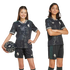 Two children wearing matching black soccer kits with subtle floral patterns and green details. One child holds a soccer ball.