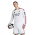 A man in a white Real Madrid long-sleeve jersey and shorts holds a soccer ball against a plain white background.